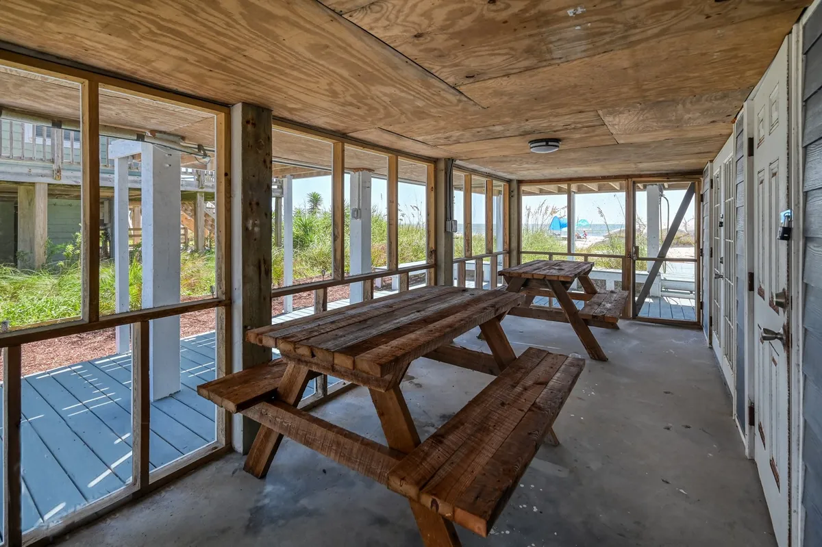 A spacious interior with wooden picnic tables, large windows offering views of outdoor greenery, and abundant natural light. The setting is relaxed and communal, inviting families to gather for snacks or crafts after outdoor adventures.