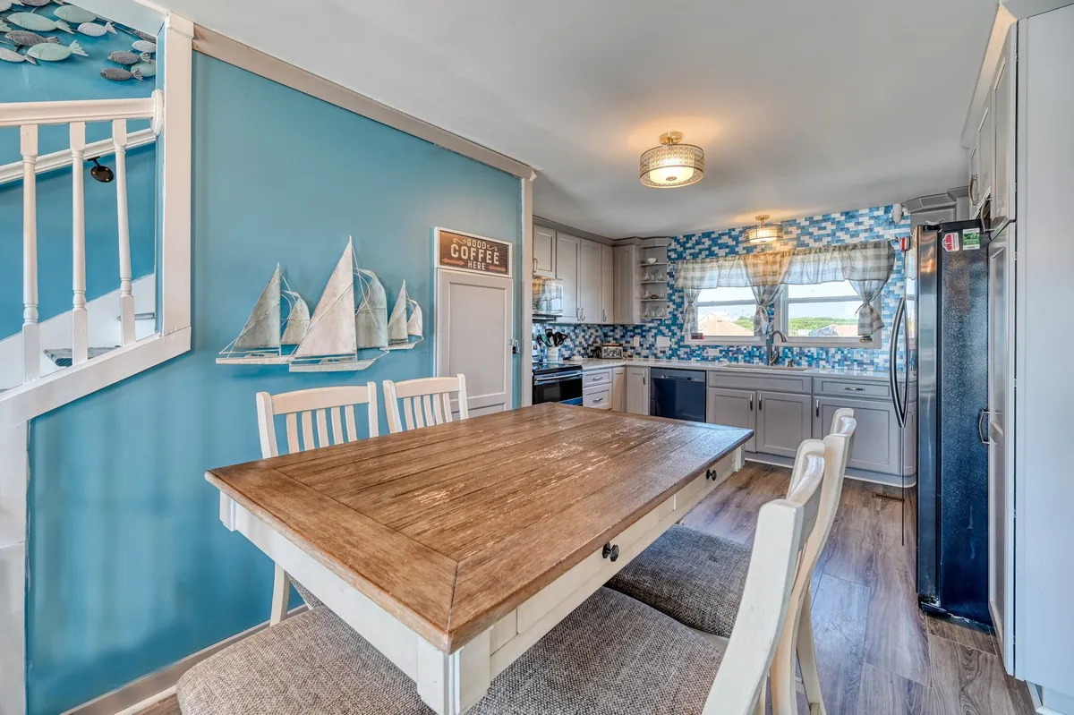 A dining table sits at the heart of the home, accented by a blue wall with thoughtful decor and visible kitchen appliances nearby. The scene suggests a welcoming spot for group meals, coffee chats, or celebrations.