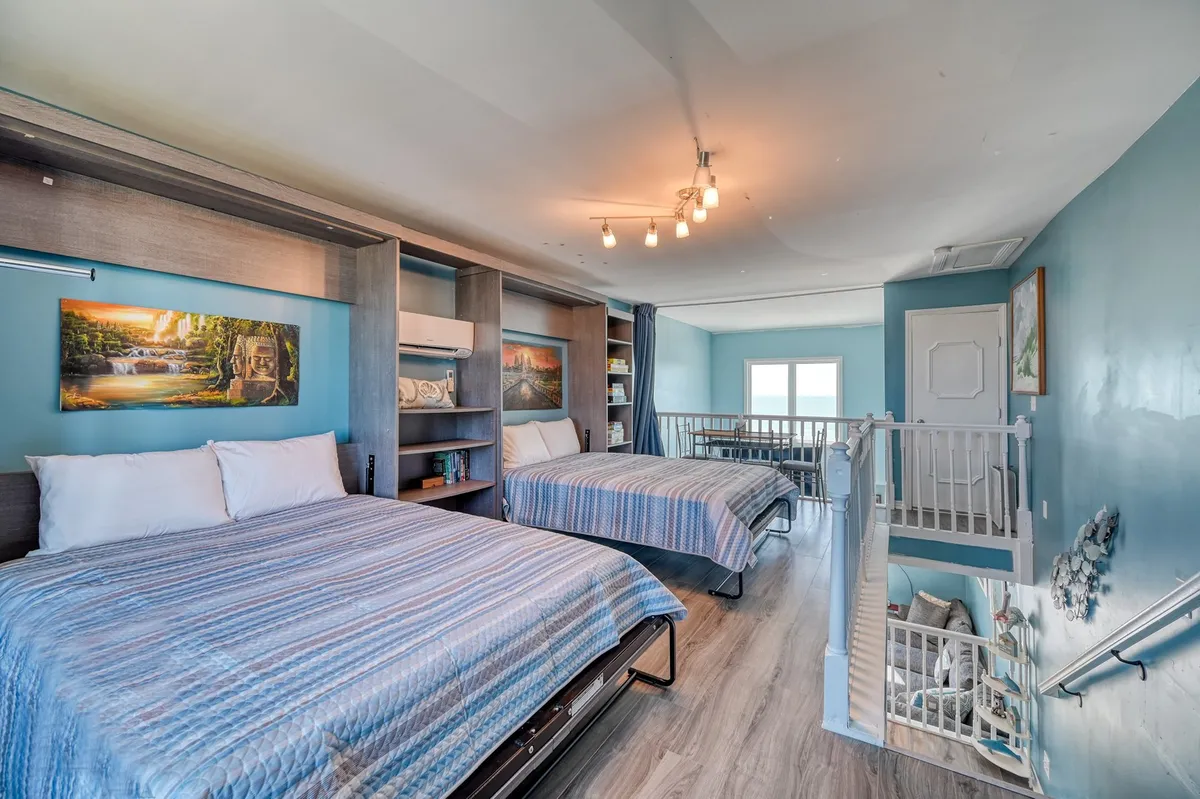 A welcoming loft space with two large beds, a bookshelf filled with books, and decorative wall art. The mood is comfortable and inviting, ideal for relaxation, reading, or socializing. The layout suggests a flexible space for different group types.