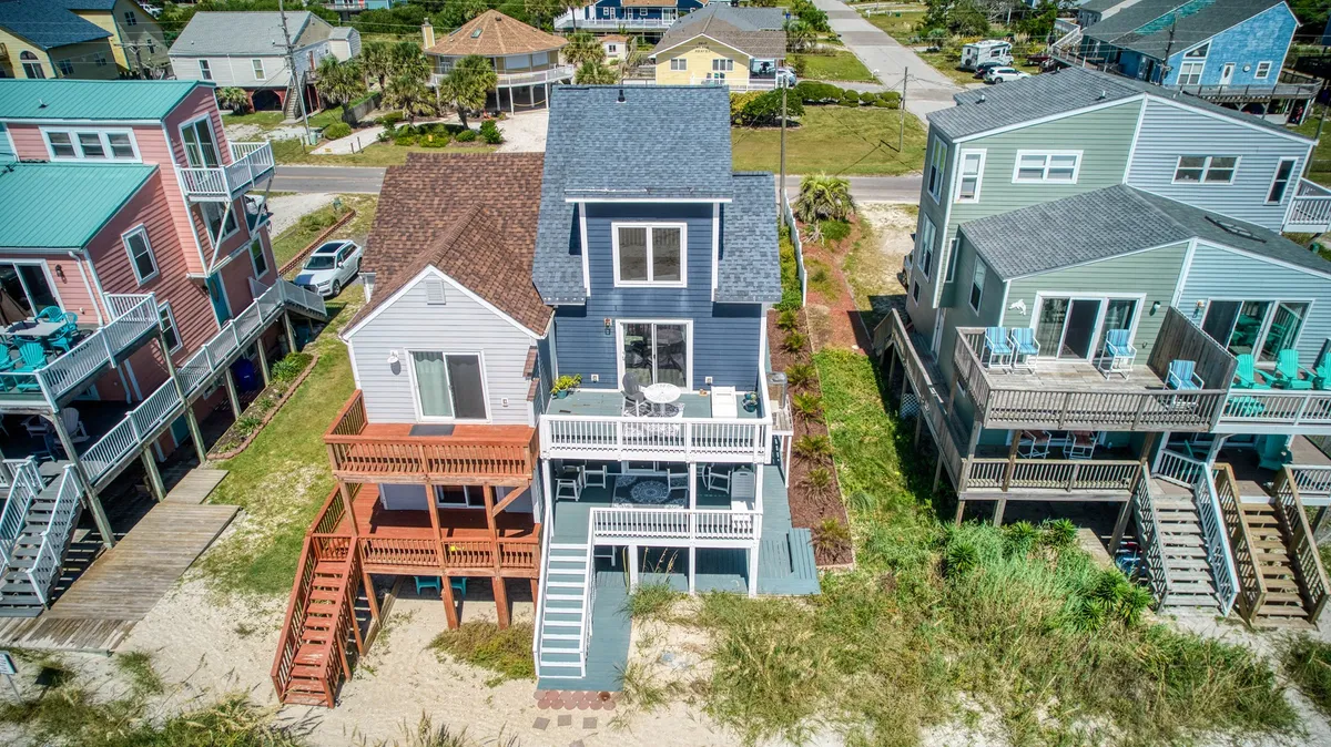 A cheerful exterior shot of colorful houses, spacious decks, and a landscaped yard. The deck areas are ideal for relaxing with family (and pets), socializing, or enjoying the ocean view together after a day on the sand.